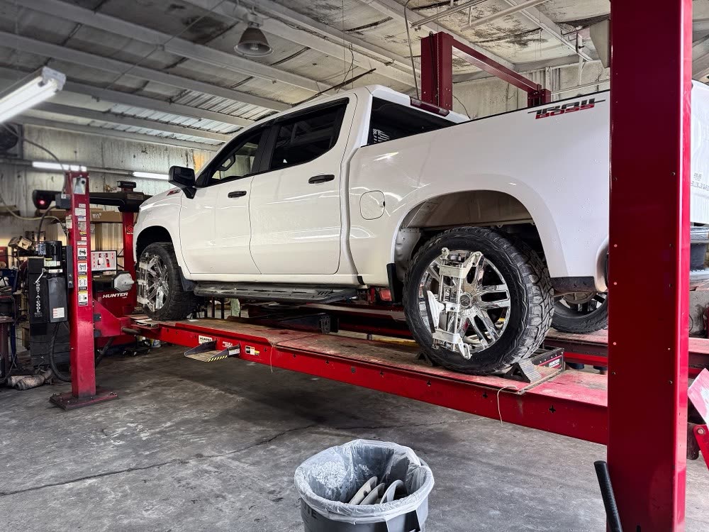 A white pickup raised on a red alignment rack inside a Garrett Automotive bay